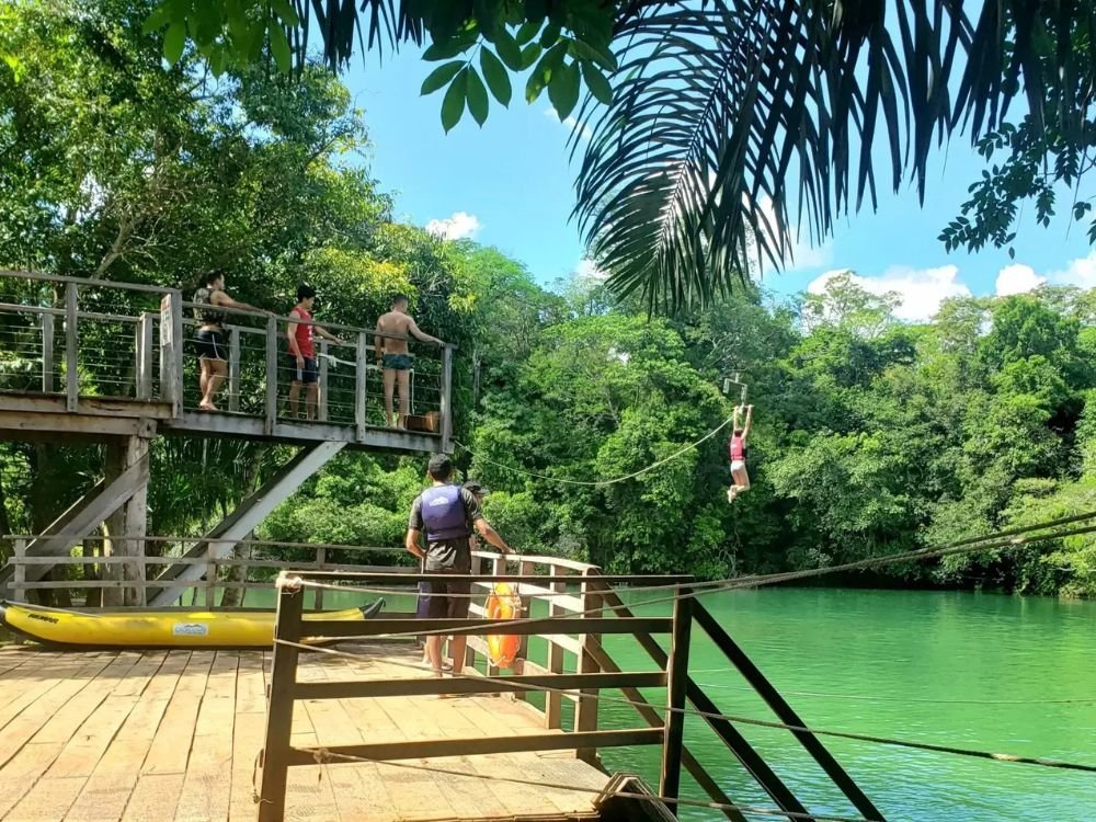 Turistas em tirolesa sobre rio cercado por vegetação nativa, atração de aventura para quem planeja quantos dias ficar em Bonito MS.